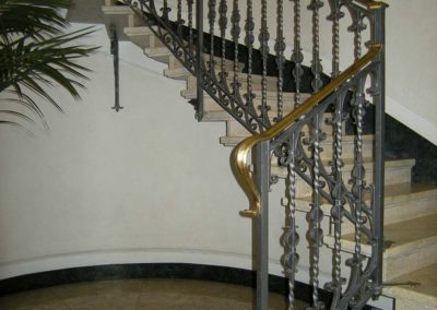 Partenza della scala in ferro battuto con motivi verticali e riccioli e corrimano in ottone in palazzo Luxottica a Milano